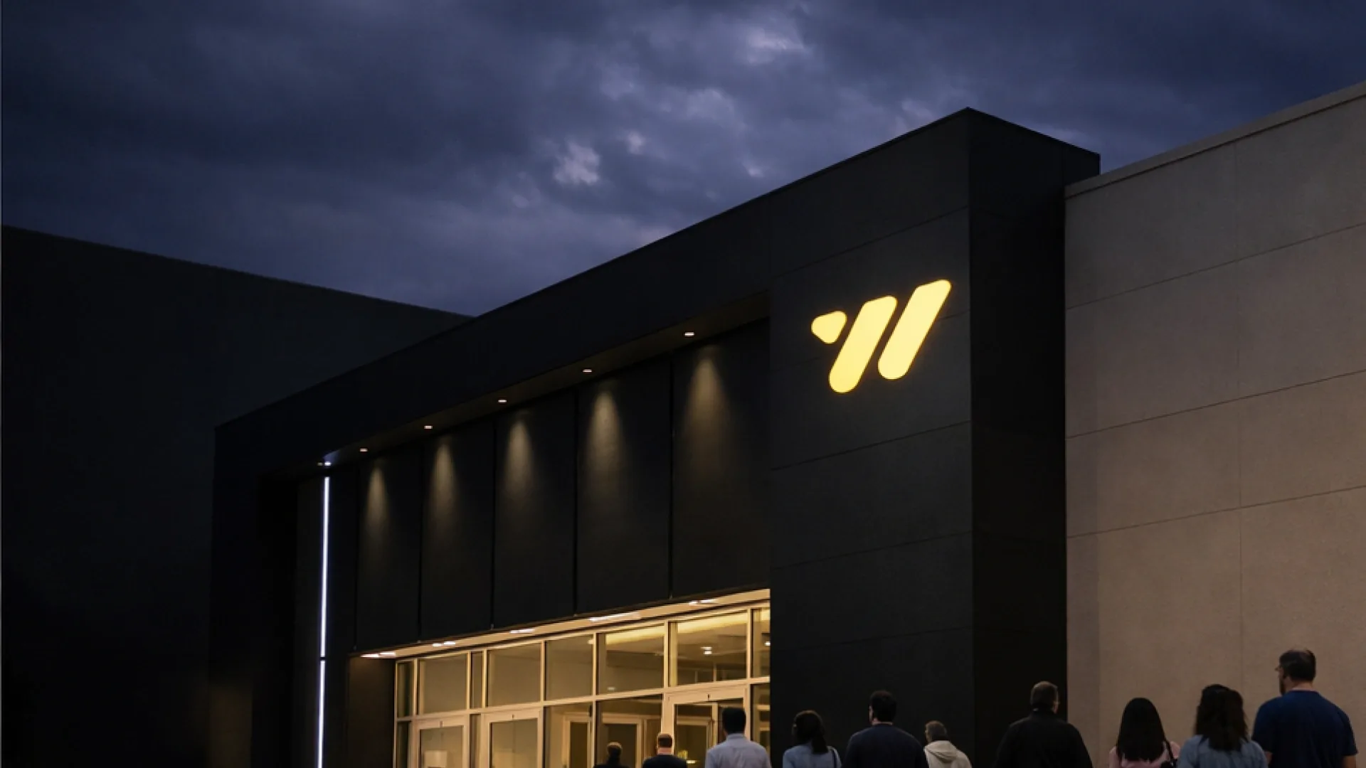 A modern theatre building at dusk, the glowing yellow Weston W mark above the entrance as people walk in
